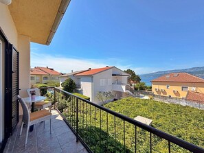 A balcony with a table and chairs, a view of neighboring houses, and a clear sky.