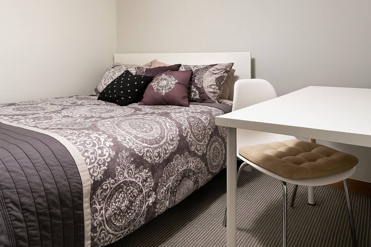 A neatly arranged bedroom with a bed, a white table, and a chair.