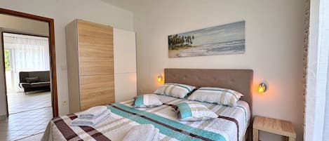 A bedroom with a bed, bedside lamps, a painting, a wooden bench, and a view of a balcony.