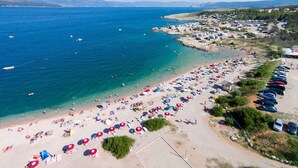 An aerial view of a beach with numerous umbrellas and people, a clear blue sea, and a parking area with cars. - Apartment Nikolic - balcony, quiet area, garden, supermarket (Šilo)