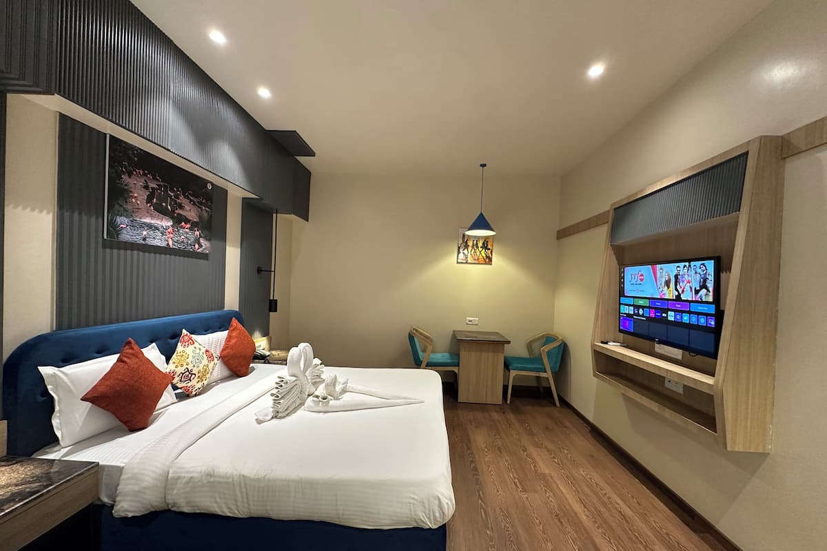 A hotel room with a bed, a desk, a TV, and a wall-mounted shelf.