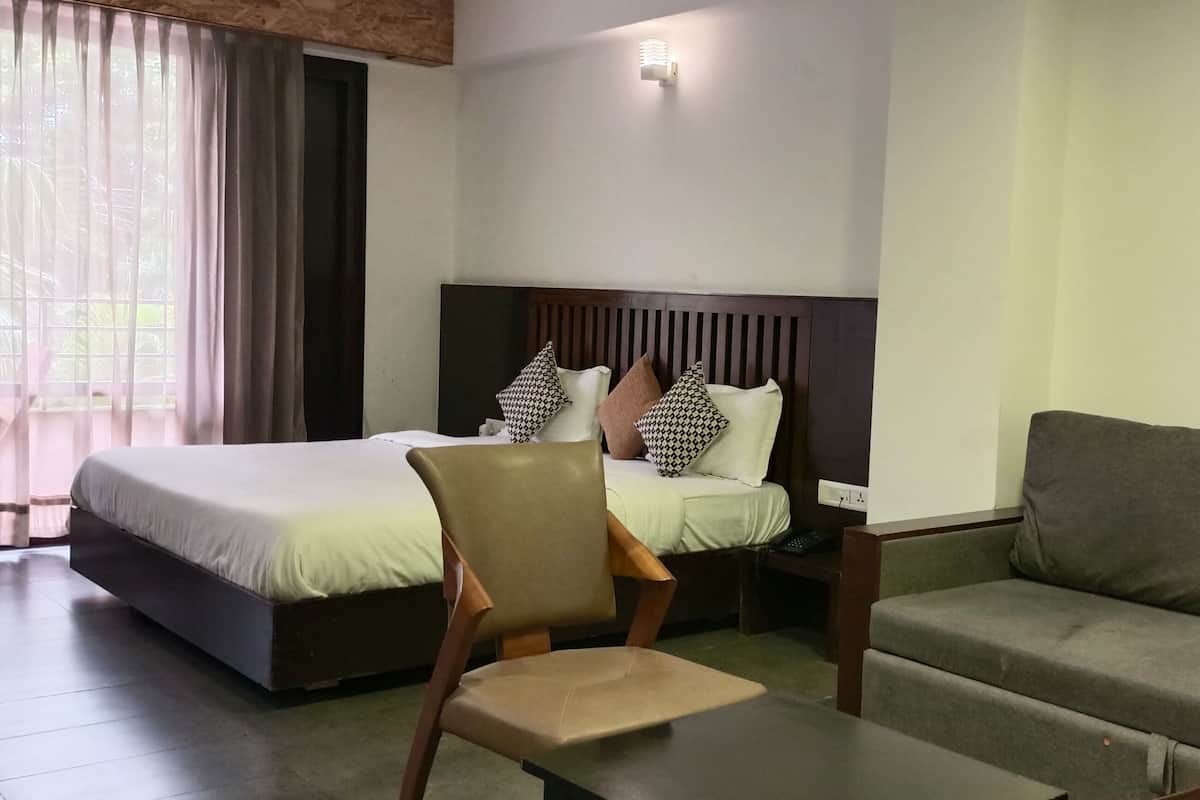 A hotel room with a bed, a chair, a sofa, and a window with curtains.