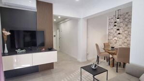 Una sala moderna con televisor de pantalla plana, un comedor con mesa de vidrio y una pared decorativa con estampado floral.
