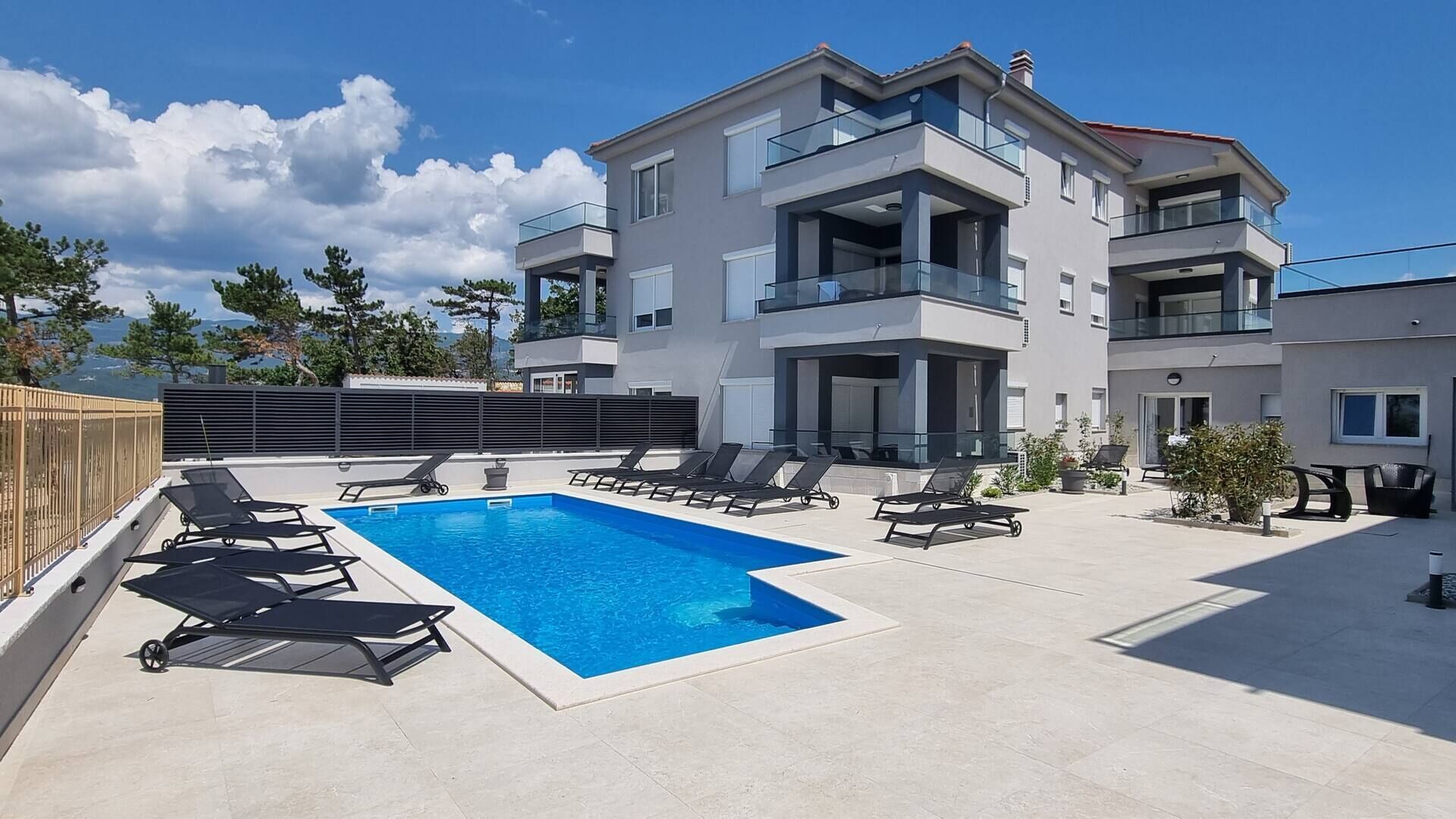 Un immeuble d’appartements moderne doté d’une piscine sur le toit, comprenant des chaises longues et une piscine à l’eau d’un bleu cristallin.