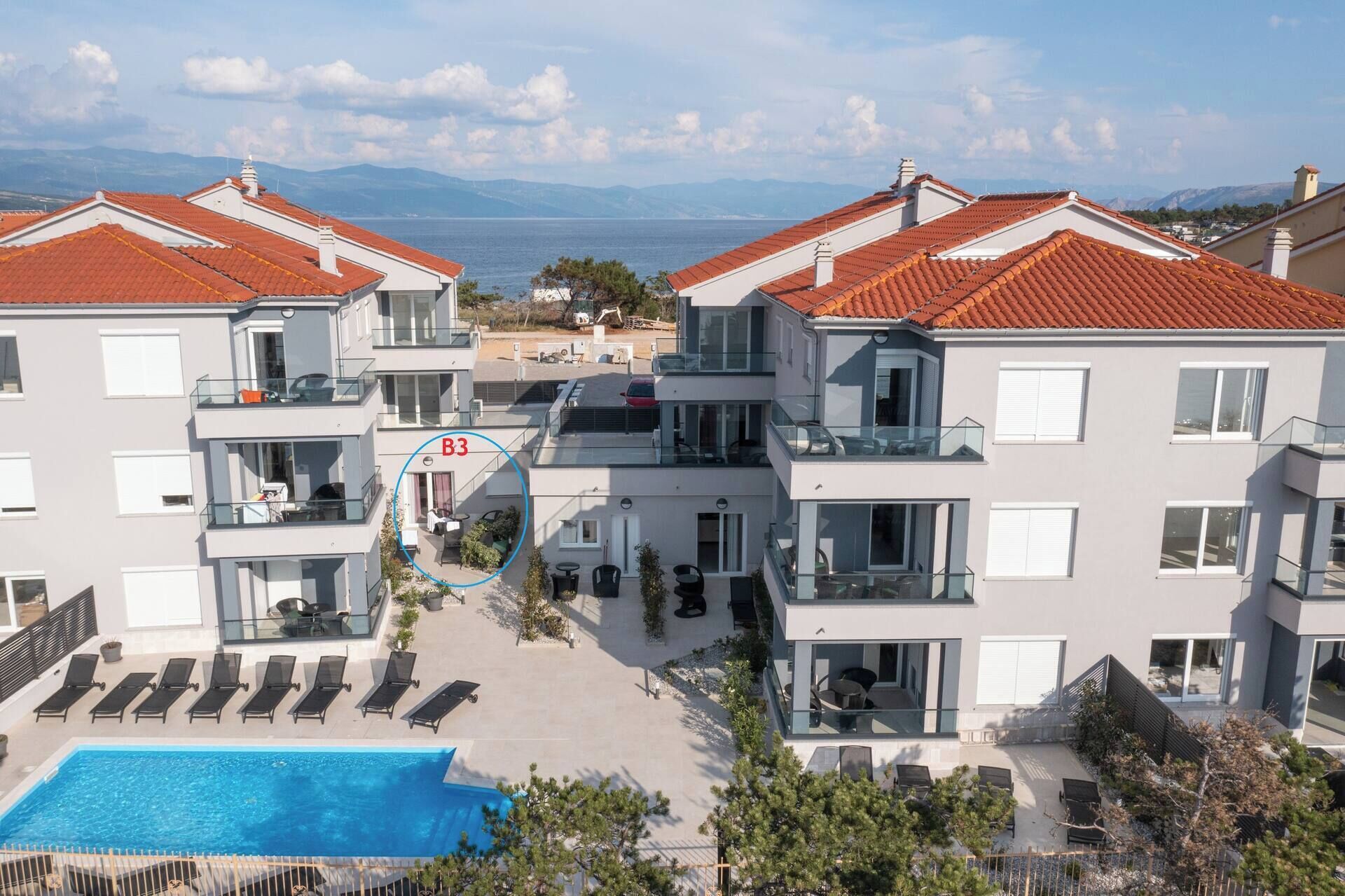 A modern apartment complex with a swimming pool, balconies, and a view of the sea.