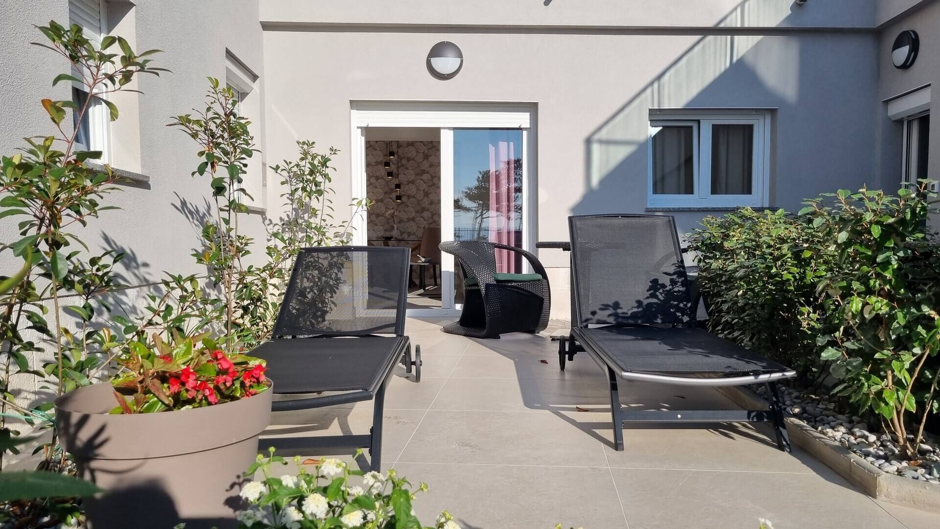 Una terrazza esterna con due poltrone, una pianta in vaso con fiori rossi e un tavolino.