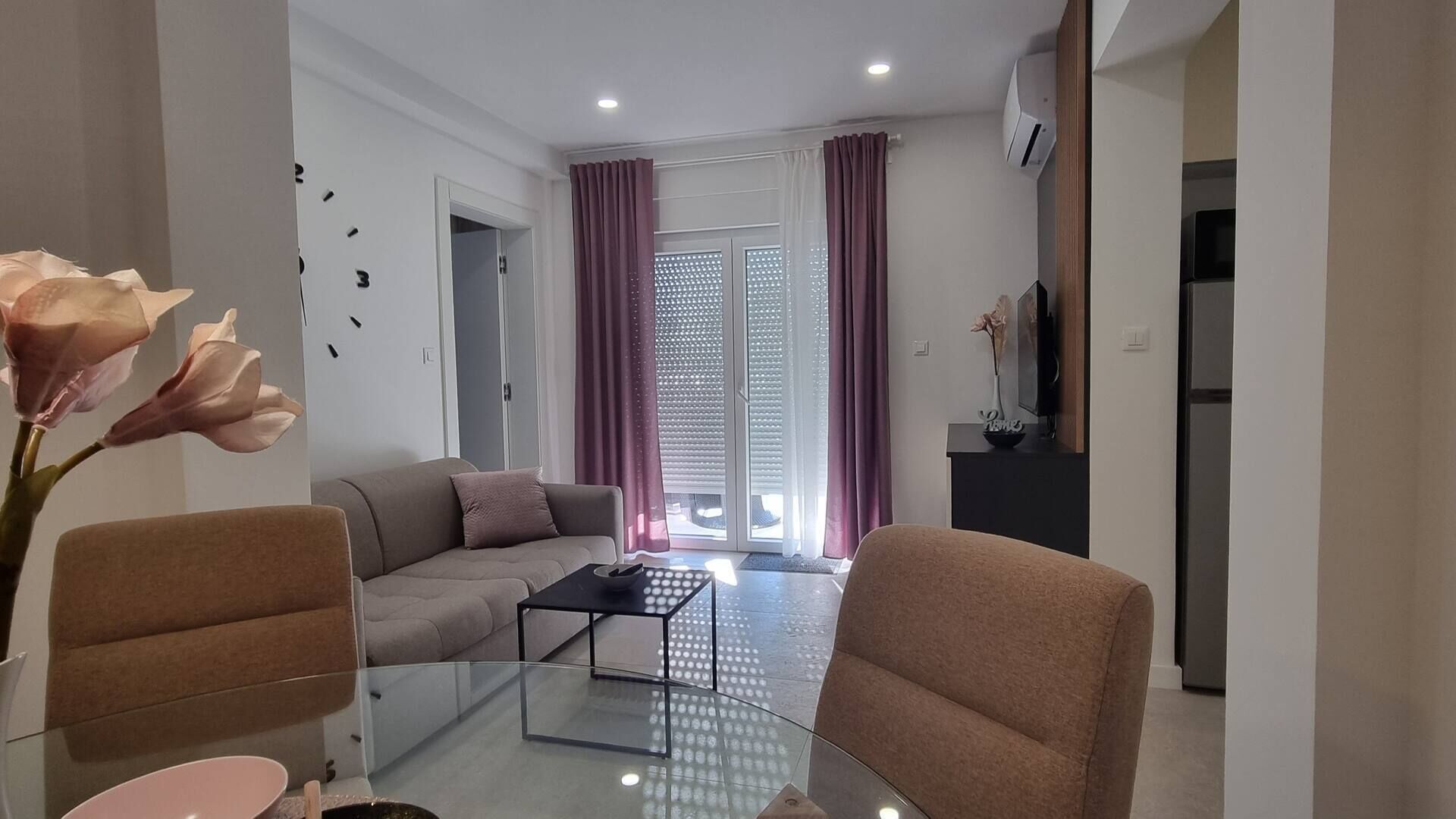 A modern living room with a sofa, armchairs, a glass coffee table, and a sliding glass door leading to a balcony.