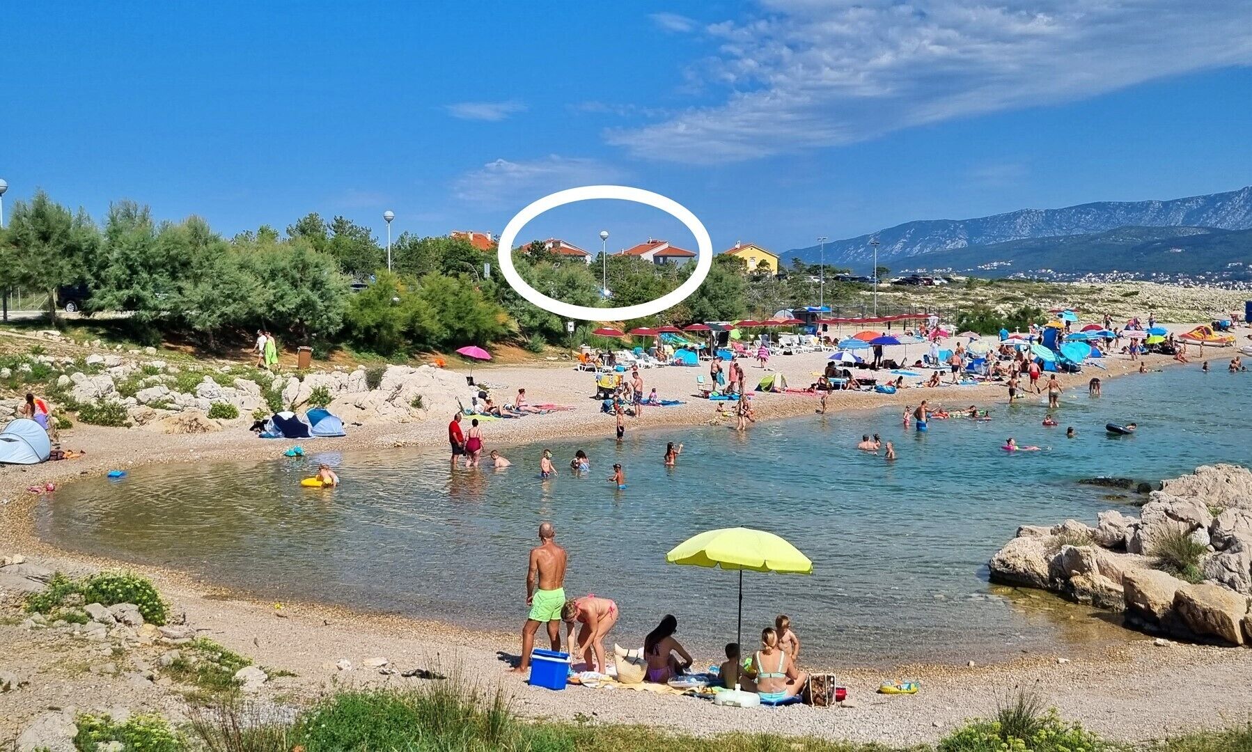 Una playa con gente nadando y tomando el sol, tiendas de campaña y sombrillas.