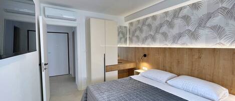 Un dormitorio con cama, armario, espejo y pared con diseño de hojas.