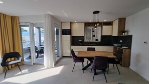 A modern kitchen with a dining area, a sliding glass door leading to an outdoor patio, and a small island with a sink. - Luxury Apartments Punta Silo - 30 m from the sea, sea view, swimming pool, outdoor shower, Smart TV, laundry room, private parking (Šilo)