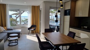 Uma sala de estar moderna com sofá, mesa de jantar com cadeiras, área de cozinha e janelas amplas com cortinas.