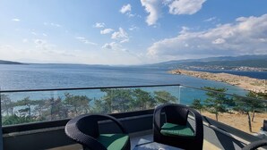 Un balcón con sillas de mimbre y una mesa, con vista a la costa, una playa y montañas distantes.