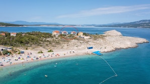 Zona costera con playa, una península rocosa y un pequeño grupo de edificios con tejados rojos.