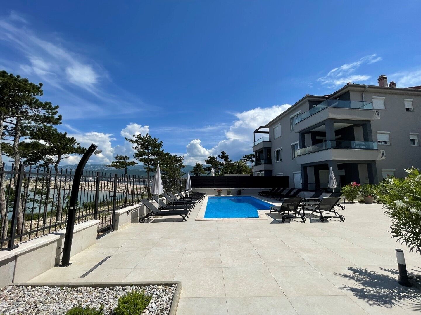 Un bâtiment moderne doté d’une piscine et de chaises longues, entouré d’une clôture et d’arbres.