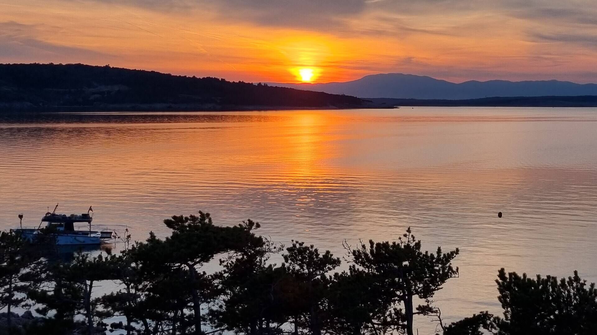 Un atardecer sobre un lago tranquilo con un bote amarrado a la izquierda y árboles en primer plano.