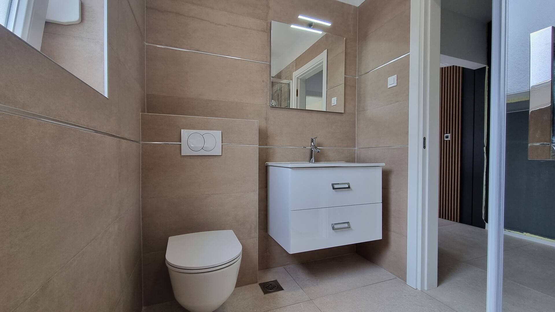 Une salle de bain moderne comprenant des toilettes, un lavabo avec un miroir et un espace douche.