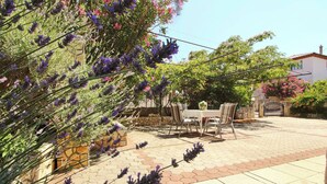 Un patio al aire libre con una mesa y sillas, rodeado de plantas de lavanda y un muro de piedra.