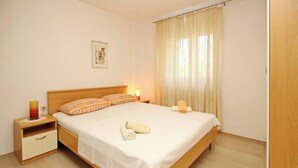 Un dormitorio ordenado con cama, mesitas de noche, una lámpara, una toalla y una cortina.