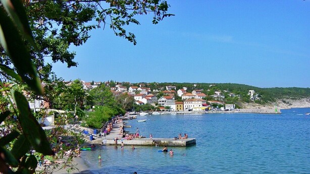 Eine Küstenstadt mit Strand, klarem blauen Wasser und Häusern im Hintergrund.
