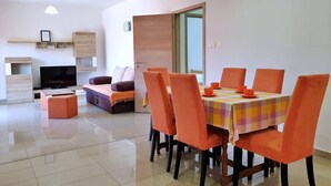 A modern living room with a sofa, TV, and dining area with orange chairs and a checkered tablecloth. - Apartment Rea - 220 m from sea, pet-friendly, private parking, terrace (Šilo)