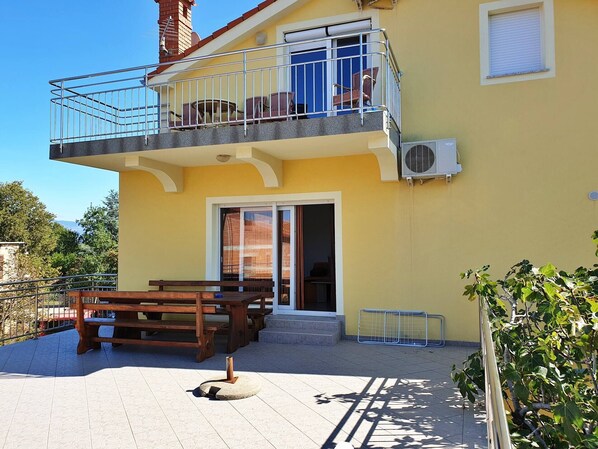 A two-story building with a balcony, a wooden bench, and a door leading to an interior space. - Apartment Rea - 250 m from sea, pet-friendly, private parking, terrace (Šilo)