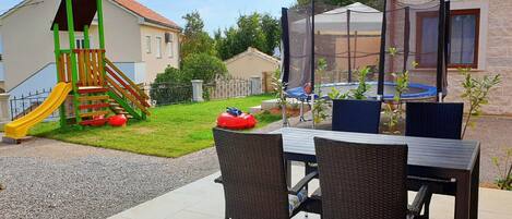 A patio area with a table and chairs, a children's play structure, and a trampoline.