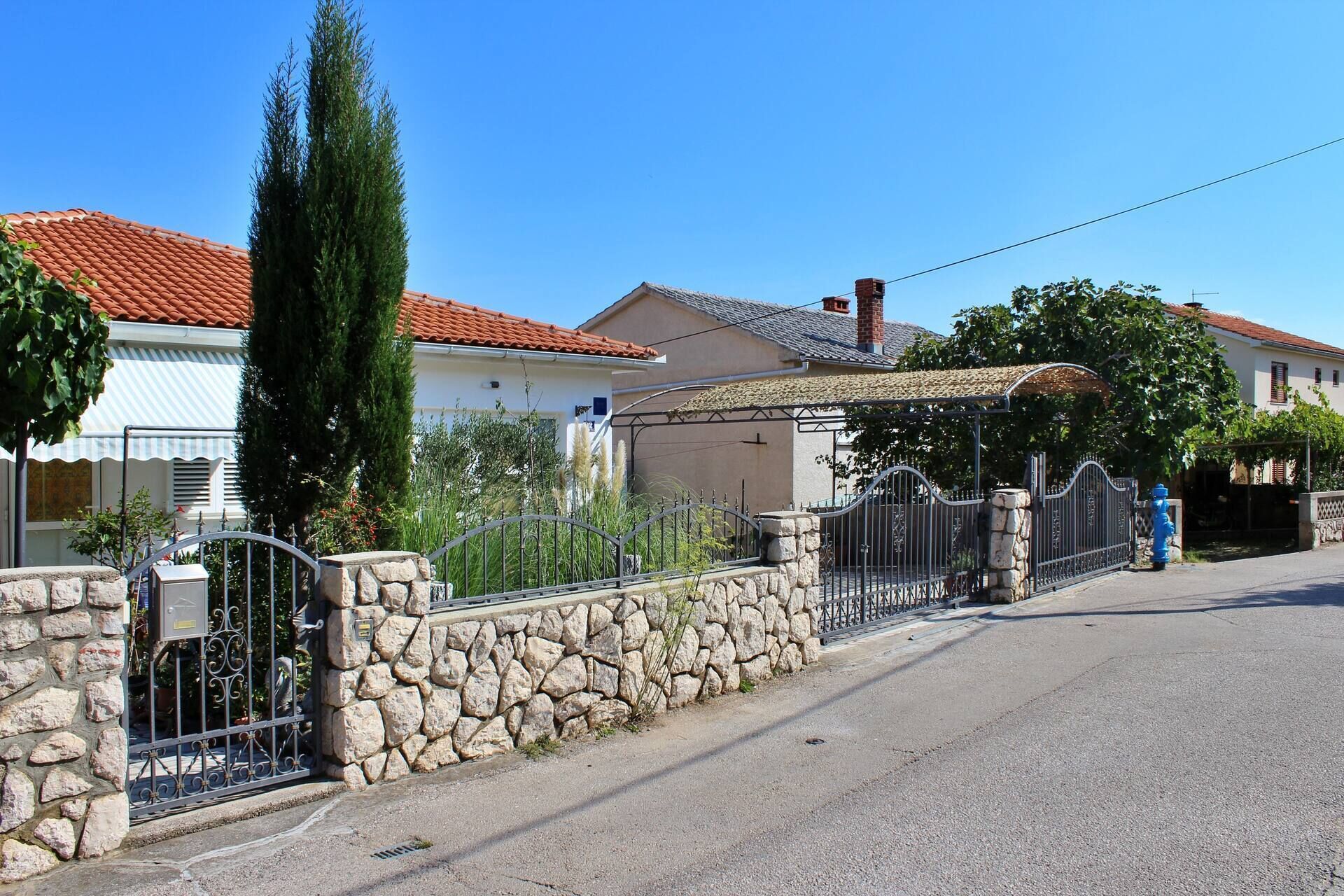 A residential street with houses, a stone wall, and a metal gate.