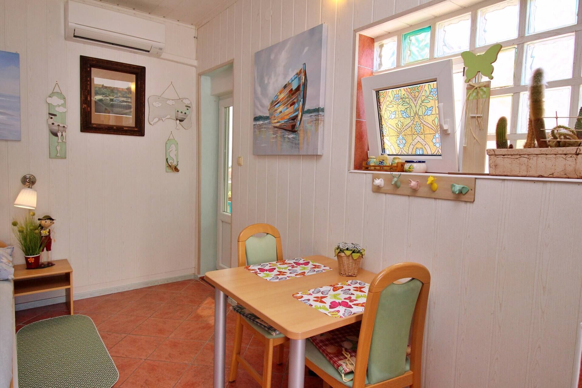 A dining area with a wooden table and chairs, a window with a view, and wall decorations including paintings and a cactus.