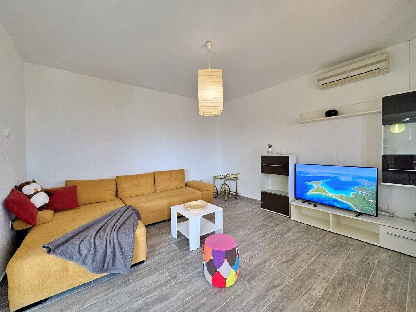 A modern living room with a sofa, a TV, a small table, and a colorful stool.