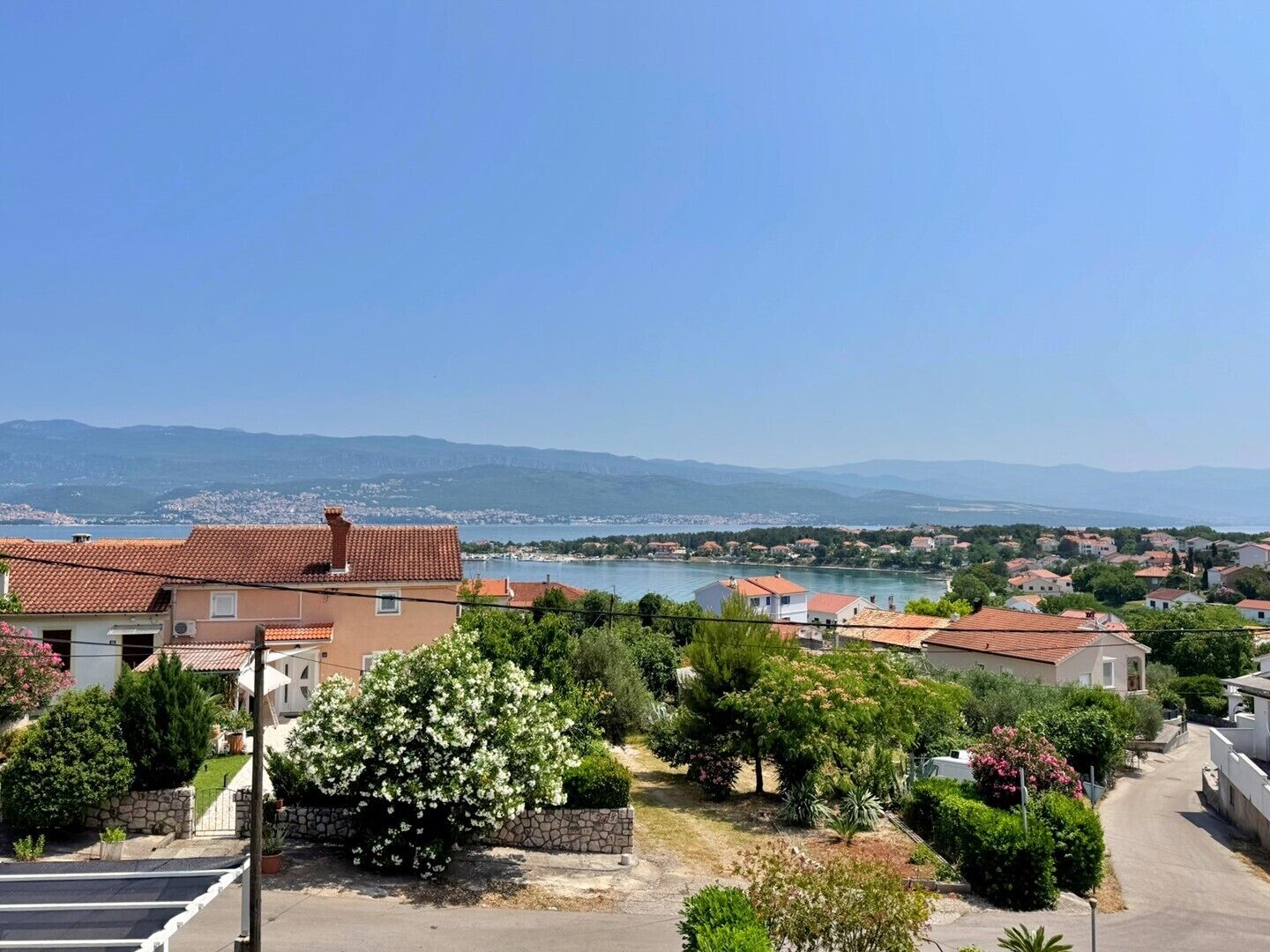 A residential area with houses, a clear view of the sea, and a mountainous backdrop.