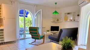 A modern living room with a sofa, a dining table, a green chair, a TV, and a potted plant. - Apartment Savic - 90 m from the sea, private terrace, air conditioning, private parking, near the sandy beach (Šilo)