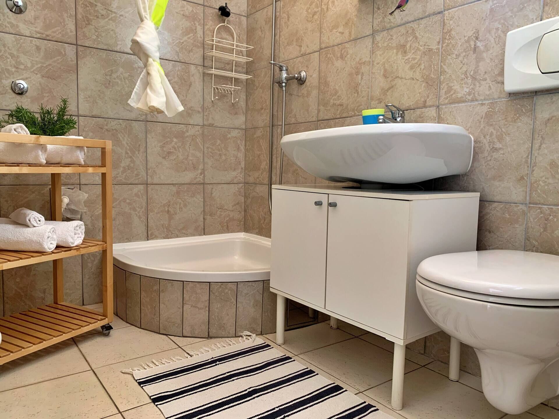 Une salle de bain moderne équipée d’une baignoire, de toilettes, d’un lavabo et d’une étagère en bois où sont posées des serviettes.