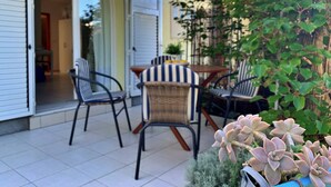 An outdoor patio with a table and chairs, a small garden area with plants, and a building entrance with a door and window. - Apartment Savic - 90 m from the sea, private terrace, air conditioning, private parking, near the sandy beach (Šilo)