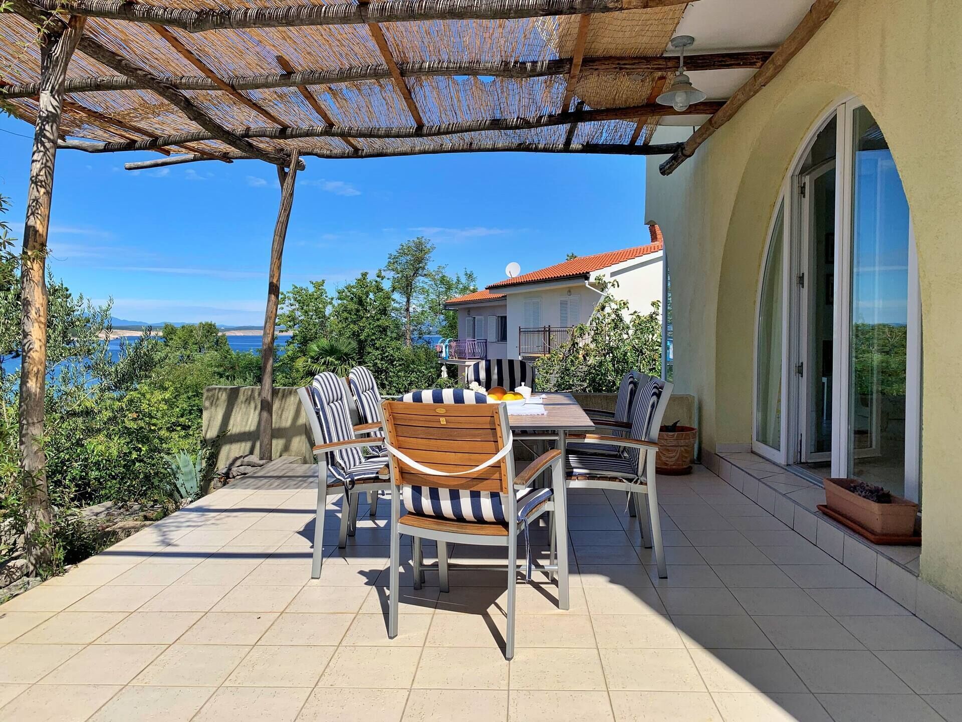 Een terras met een tafel en stoelen, een pergola en uitzicht op zee.