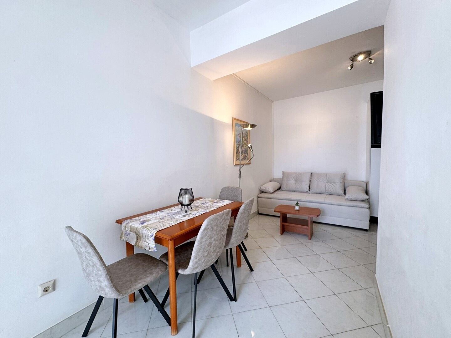 A dining area with a wooden table, four chairs, and a sofa in the background.