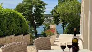 A terrace with wicker chairs, a table, and a bottle of wine. - Apartment Scheich - seafront, 20 m from sea, ground floor, terrace (Šilo)