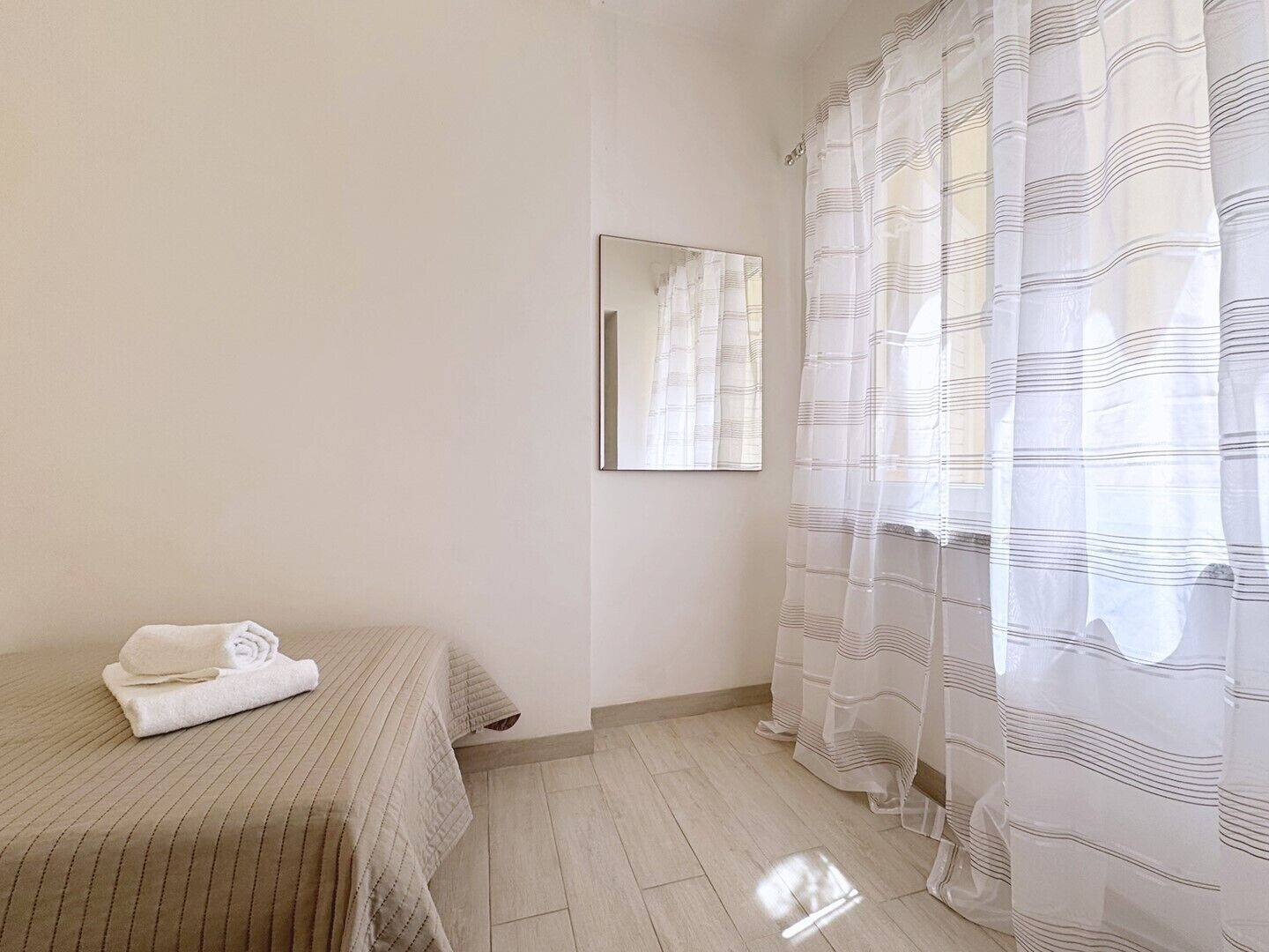 Un dormitorio con una cama, una toalla doblada, un espejo y una ventana con cortina a rayas.