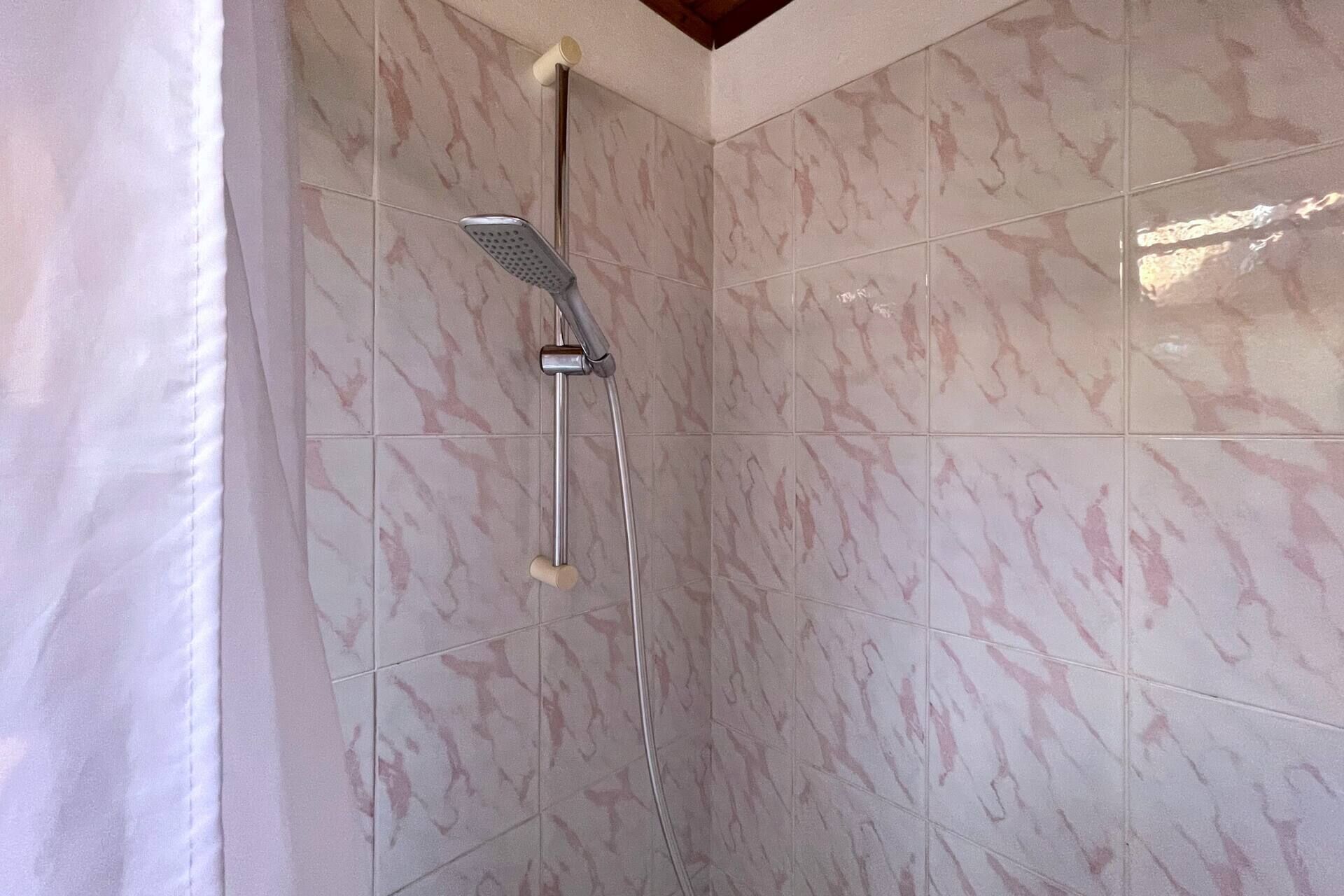 Une douche équipée d’un pommeau de douche à main et d’un robinet fixé au mur.