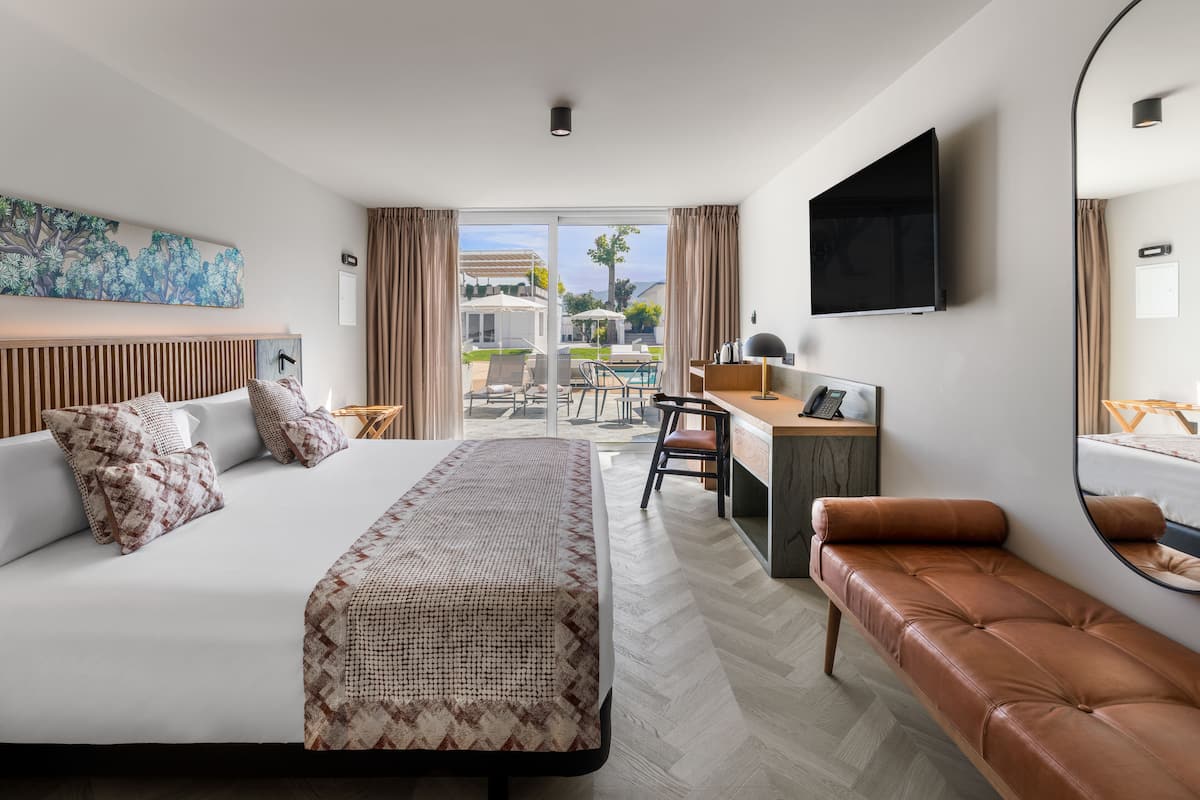 Ein Hotelzimmer mit Bett, Schreibtisch, Laptop, Fernseher und Blick ins Freie.