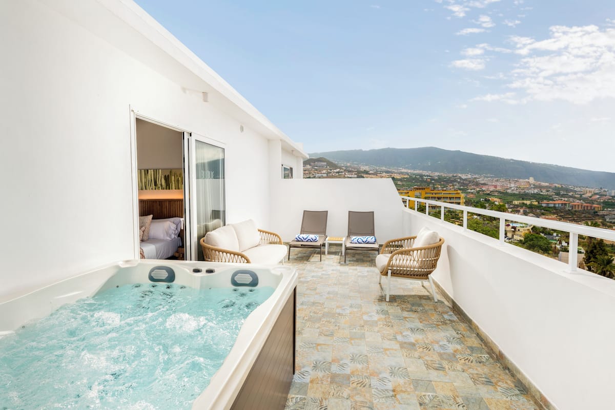 Ein Balkon mit Whirlpool, zwei Korbstühlen und Blick auf die Stadt.