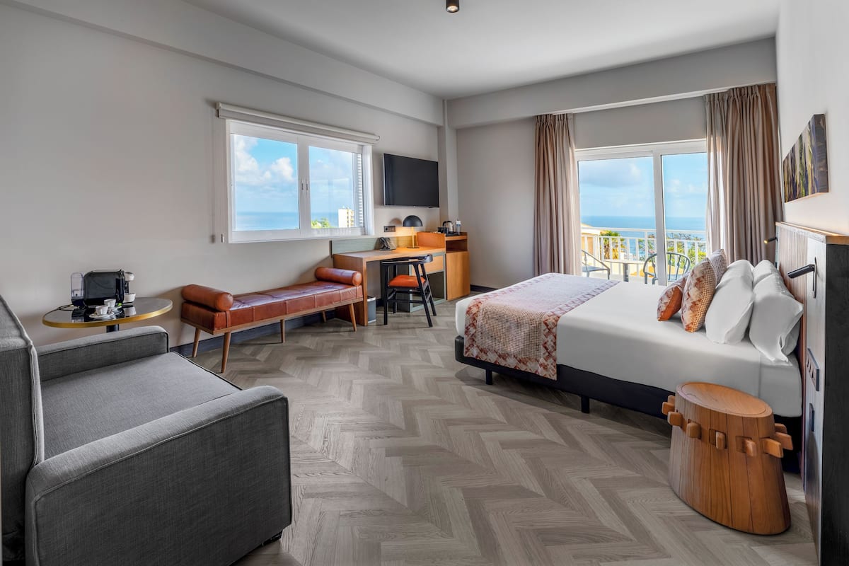 Ein Hotelzimmer mit einem Bett, einem Schreibtisch, einem Sessel, einer Couch und einem Fernseher.