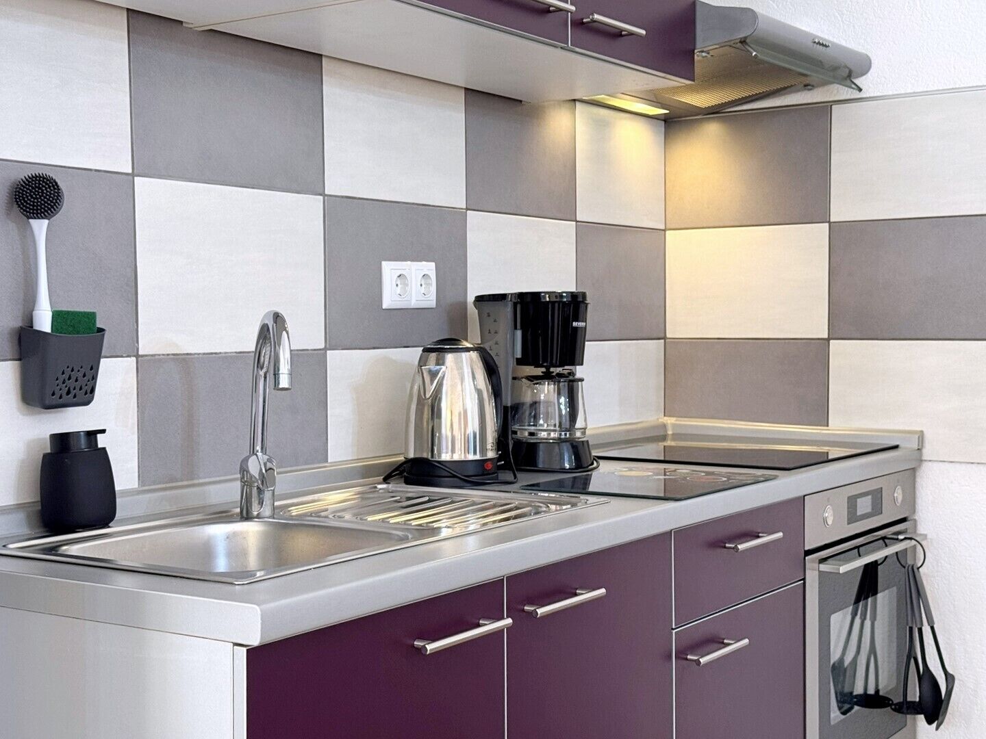 A modern kitchen with a stainless steel sink, a kettle, and a coffee maker.