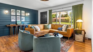 Una sala de estar moderna con un sofá modular, dos sillones, una mesa de centro y una mesita auxiliar. Hay marcos de cuadros en la pared y una lámpara colgante.