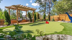 Una pérgola de madera con sillas colgantes, un pequeño campo de golfito y una estatua de dinosaurio.