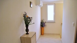 Un couloir avec une armoire en bois, deux vases de fleurs, une fenêtre et un sol carrelé.