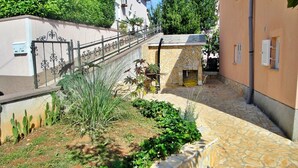 Une cour avec un chemin en pierre, un jardin de cactus et un petit bâtiment en pierre doté d’une rambarde en métal.