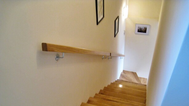 Un escalier en bois avec une rampe, des murs blancs et un petit tableau accroché au mur.
