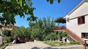 Une cour dallée avec un sol en pierre, entourée d’arbres et bordée d’un bâtiment doté d’un escalier rouge.