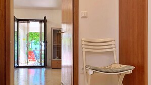 Une pièce avec une chaise blanche, un meuble en bois et une porte en verre donnant sur un espace extérieur.