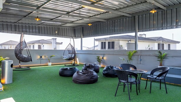 An outdoor seating area with artificial grass, black bean bags, wicker chairs, and hanging chairs. - Housr Benson Marathahalli Bangalore (Bengaluru)